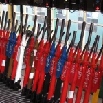 Rows of red, blue and white railway signal levers with numbered name plates inside a signal box, with a train visible through the windows
