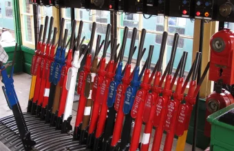 Rows of red, blue and white railway signal levers with numbered name plates inside a signal box, with a train visible through the windows
