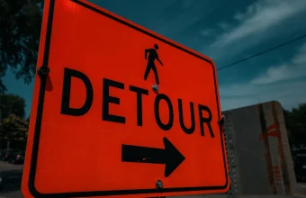 An orange DETOUR road sign with a pedestrian symbol and a right-pointing arrow against a dark blue sky