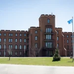 Exterior of Building 1 on the Department of Homeland Security’s St. Elizabeths campus in Washington, D.C., a red brick building with a central tower and flagpoles under a blue sky