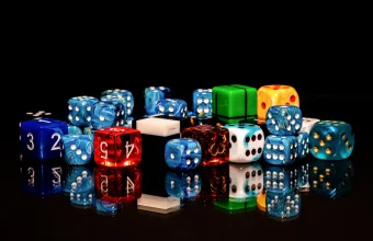 A pile of colorful six-sided and polyhedral dice with reflections on a black glossy surface