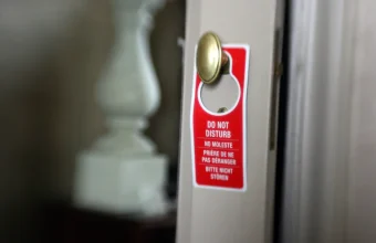 Red hotel door hanger reading Do Not Disturb in four languages on a brass doorknob, a request that does not lock the door
