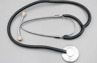 A black-tubed stethoscope with cream ear tips and a steel chest piece laid flat on a light gray surface