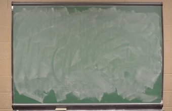 A green classroom chalkboard wiped almost clean, with pale smears of chalk where earlier writing was erased
