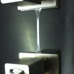 A thin transparent polymer test specimen stretched between the metal grips of a tensile testing machine