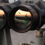 Large naval binoculars whose two lenses each reflect the same sunset scene of a ship and a helicopter