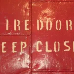 Red steel fire door stenciled FIRE DOOR KEEP CLOSED in cream letters