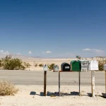 A row of roadside mailboxes on posts beside a desert road, with a red STOP sign at the left edge