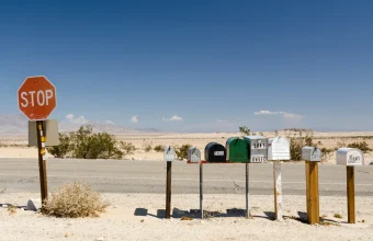 A row of roadside mailboxes on posts beside a desert road, with a red STOP sign at the left edge
