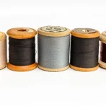 Five wooden sewing-thread spools in different colors lined up side by side on a white background