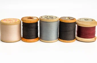 Five wooden sewing-thread spools in different colors lined up side by side on a white background