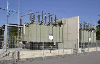 A tall concrete fire wall between two large transformers behind a metal fence at the Kachlet power station in Passau, Germany