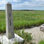 Granite border marker obelisk inscribed United States Treaty 1925 beside a bronze plaque on open prairie at the Canada and United States border