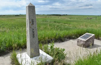 Granite border marker obelisk inscribed United States Treaty 1925 beside a bronze plaque on open prairie at the Canada and United States border