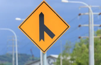 Yellow diamond-shaped merging traffic warning sign showing a side road joining a main road