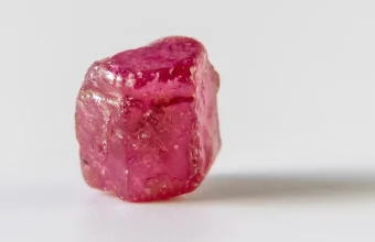 A raw, uncut ruby crystal with a glossy pink-red surface on a plain white background