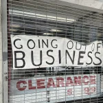 Handwritten Going Out of Business banner hung on a closed metal shop shutter above a Clearance sign