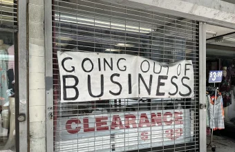 Handwritten Going Out of Business banner hung on a closed metal shop shutter above a Clearance sign