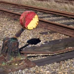 A rusted railway switch lever with a red and yellow signal disc beside a railway track