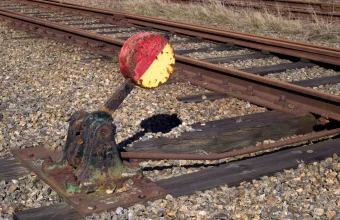 A rusted railway switch lever with a red and yellow signal disc beside a railway track