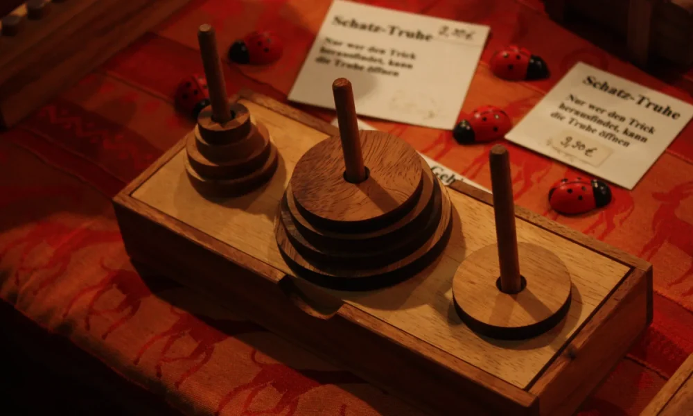 A wooden Tower of Hanoi puzzle on a market table, with three pegs and stacked discs of different sizes