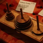 A wooden Tower of Hanoi puzzle on a market table, with three pegs and stacked discs of different sizes