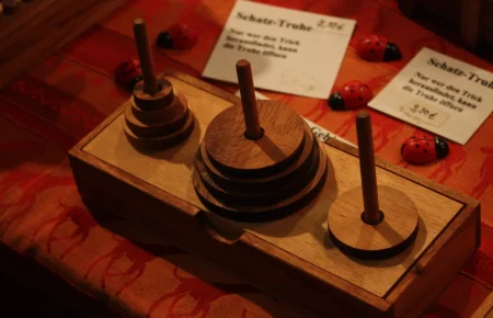A wooden Tower of Hanoi puzzle on a market table, with three pegs and stacked discs of different sizes