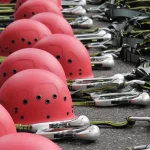 Rows of red climbing helmets, carabiners and harness straps laid out on the ground at a ropes course