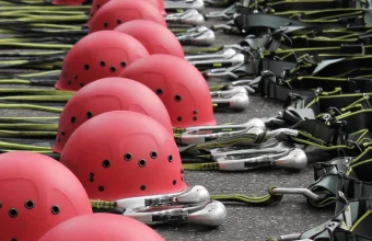 Rows of red climbing helmets, carabiners and harness straps laid out on the ground at a ropes course