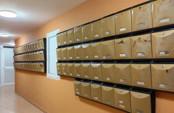 Rows of identical brass-colored apartment mailboxes with small locks and name labels along an orange corridor wall