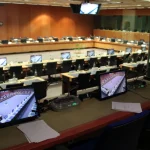 An empty interpreters booth with a microphone console and monitors overlooking a large Council meeting room in Brussels