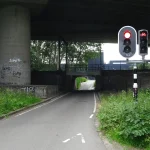A single-lane road under a railway bridge in Rotterdam where traffic lights show red so that only one direction passes at a time