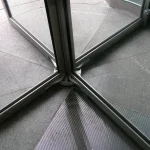 Base of a revolving door seen from above, with glass panels meeting at the central axis over a granite floor