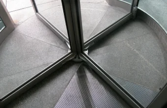 Base of a revolving door seen from above, with glass panels meeting at the central axis over a granite floor