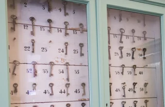 A glass-fronted green cabinet holding rows of old keys on numbered hooks, with several hooks empty