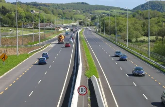 A dual carriageway seen from above, with a grass and concrete-barrier median strip separating the two carriageways and a 100 km/h speed limit sign standing on the median