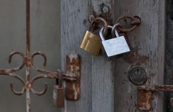 Two padlocks with interlocked shackles, one brass and one steel, securing the weathered door of an old gate