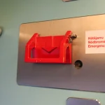 Red emergency brake handle on a brushed steel plate inside a train, with a label reading Hätäjarru, Nödbroms and Emergency brake