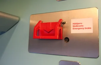 Red emergency brake handle on a brushed steel plate inside a train, with a label reading Hätäjarru, Nödbroms and Emergency brake