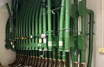 Rows of green pneumatic tubes with handwritten destination labels ending in brass outlets in the National Library of Australia’s tube system