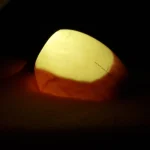 A hand holding an egg against a bright light in a dark room, with the light shining through the shell to show what is inside