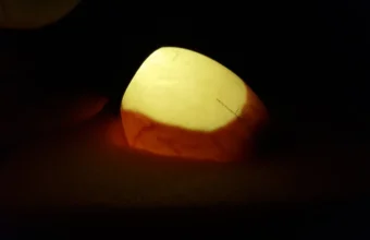 A hand holding an egg against a bright light in a dark room, with the light shining through the shell to show what is inside