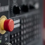 A red emergency stop button on a factory control panel, a literal kill switch