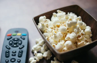 A TV remote control beside a bowl of popcorn on a dark wooden table