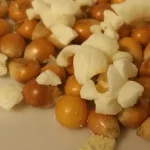 Unpopped corn kernels mixed with popped popcorn on a white surface