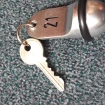 A brushed-metal hotel key fob stamped with the number 21 on a ring with a brass key, lying on grey-green carpet