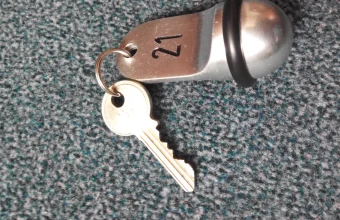 A brushed-metal hotel key fob stamped with the number 21 on a ring with a brass key, lying on grey-green carpet