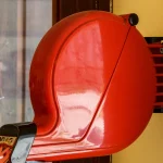 A red wall-mounted queue ticket dispenser with a ticket tab pulled out, on a yellow bakery wall