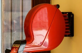 A red wall-mounted queue ticket dispenser with a ticket tab pulled out, on a yellow bakery wall