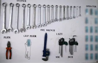 A white workshop shadow board with outlined spanners, pliers, a pipe wrench and hex keys, where an empty outline marks a tool that is missing